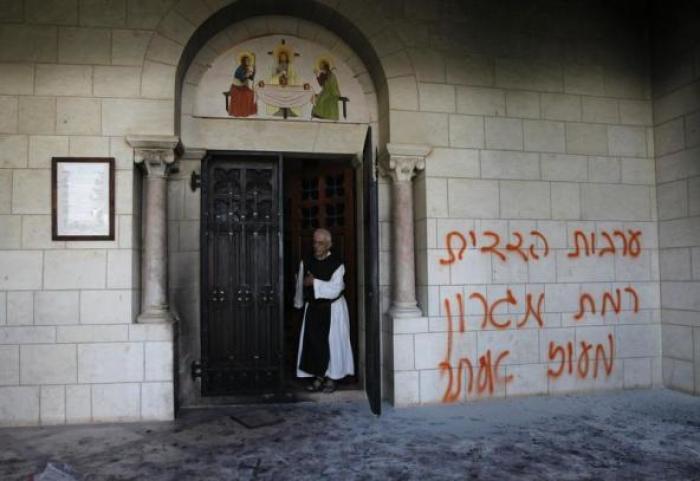 A monk stands next to graffiti sprayed by vandals on a wall at the entrance to the Latrun Monastery near Jerusalem September 4, 2012.