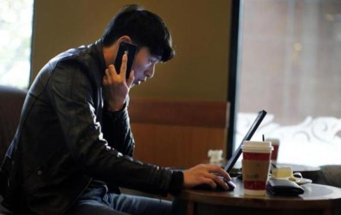 Credit : A man talks on the phone as he surfs the internet on his laptop at a local coffee shop in downtown Shanghai, China, Nov. 28, 2013.