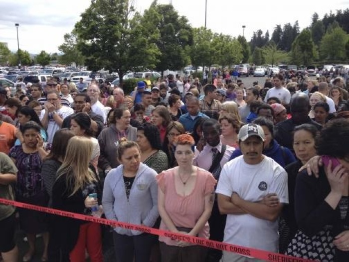 Parents wait behind police tape for students from Reynolds High School to arrive by bus in Troutdale, Oregon, June 10, 2014