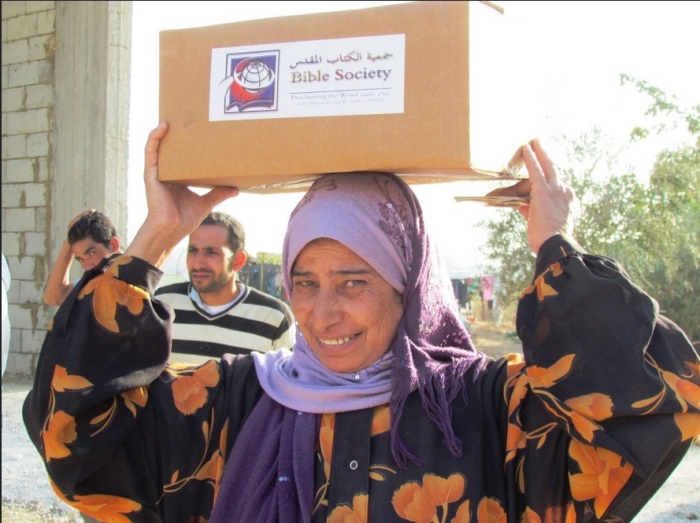 A Syrian woman smiles as she carries a Lebanon Bible Society aid package. Syrian refugee family with Lebanon Bible Society aid package. The Bible Society provides aid for around 3,000 Syrian refugee families.