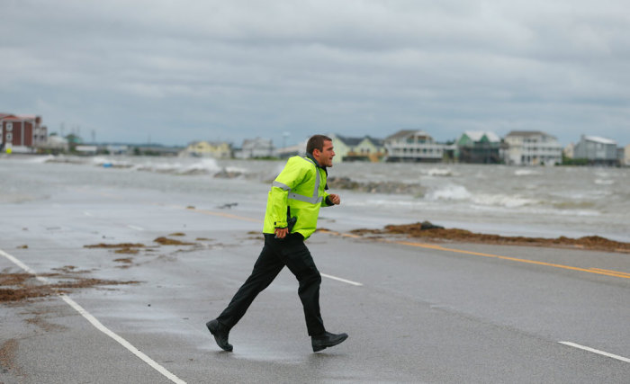 A police officer runs across the road after hurricane Arthur passed through in Nags Head, North Carolina July 4, 2014. The first hurricane of the Atlantic season has hit the North Carolina coast, a wet and windy spoiler of the July Fourth holiday for thousands of Americans as authorities ordered them to evacuate exposed areas.