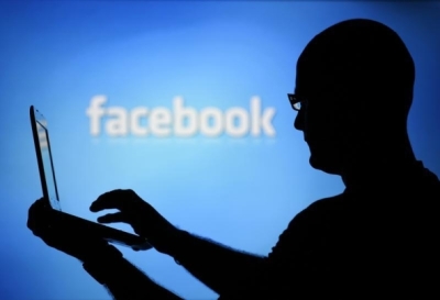 A man is silhouetted against a video screen with an Facebook logo, August 14, 2013.