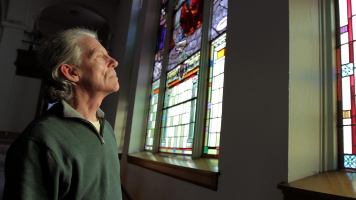Christy Wareham, pastor of Park Church in Newark, NY, stands before the church's stained glass windows. Wareham's church's attendance declined from 900 to 40 over the span of a few years.