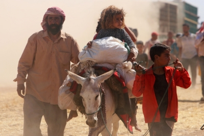 Displaced people from the minority Yazidi sect, fleeing violence from forces loyal to the Islamic State in Sinjar town, walk towards the Syrian border as others ride on a donkey on the outskirts of Sinjar mountain, near the Syrian border town of Elierbeh of Al-Hasakah Governorate August 11, 2014.