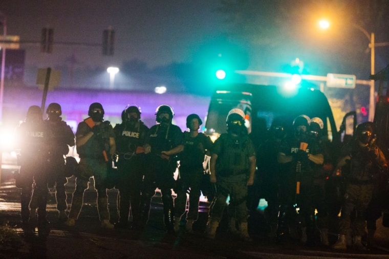 Police officers line up across the street as they maintain their distance from protesters during on-going demonstrations to protest against the shooting of Michael Brown, in Ferguson, Missouri, August 16, 2014. Protesters in Ferguson said late on Friday on Twitter that police had fired tear gas at a crowd protesting over the police shooting death of Brown, an unarmed black teen. The reported outbreak late Friday evening came after almost a week of nighttime clashes between local police and protesters saw a 24-hour break as those police forces were replaced by state police led by an African-American captain.