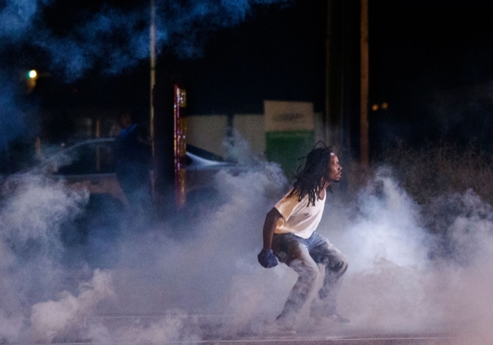 A protester yells towards police in a cloud of tear gas after protests in reaction to the shooting of Michael Brown turned violent near Ferguson, Missouri August 17, 2014. Shots were fired and police shouted through bullhorns for protesters to disperse, witnesses said, as chaos erupted Sunday night in Ferguson, Missouri, which has been racked by protests since an unarmed black teenager was shot by police last week.