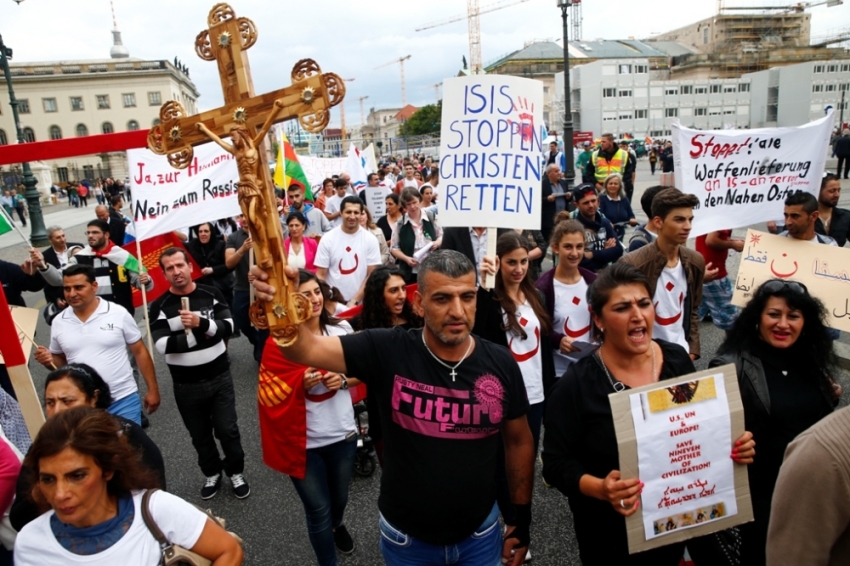 People holds crosses and signs during a rally organised by Iraqi Christians living in Germany denouncing what they say is repression by the Islamic State militant group against Christians living in Iraq, in Berlin, August 17, 2014. Some of the signs read "Stop ISIS, save the Christians" (C) and "Stop all shipment of weapons into the Middle East."