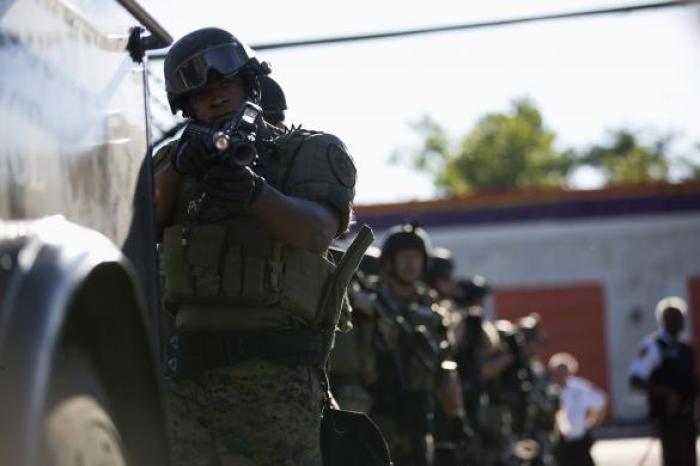 A police officer holds his riot gun while demonstrators protest the shooting death of teenager Michael Brown in Ferguson, Missouri, Aug. 13, 2014.