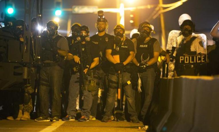 Police officers keep watch while demonstrators protesting the death of black teenager Michael Brown in Ferguson, Missouri, Aug. 12, 2014.