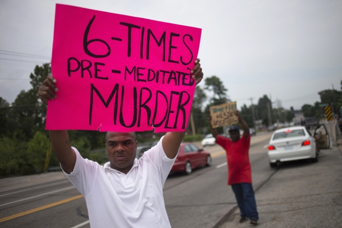 Men hold placards while demonstrating the shooting of unarmed black teenager Michael Brown along a roadside in Ferguson, Missouri, Aug. 20, 2014.