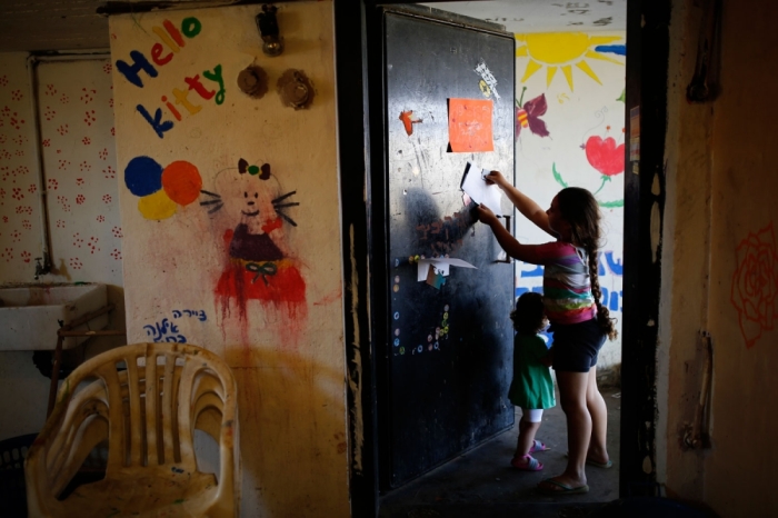 An Israeli girl hangs a drawing on the door of a public bomb shelter in the southern city of Ashkelon August 4, 2014. In Israeli southern communities hit by daily rocket and mortar bomb attacks from the Gaza Strip, some residents remained in their shelters, waiting tensely to see if a 72-hour Egyptian-brokered ceasefire that went into effect on Tuesday would hold. In Gaza, Palestinians who sheltered in U.N.-run schools began returning to towns and villages to examine the widespread damage from four weeks of fierce fighting. Picture taken August 4, 2014.