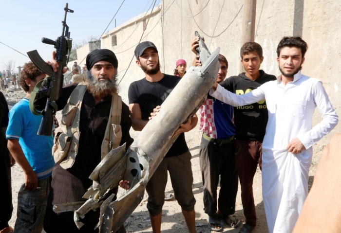 An Islamic State militant (L) stands next to residents as they hold pieces of wreckage from a Syrian war plane after it crashed in Raqqa, in northeast Syria, Sept. 16, 2014. The Syrian war plane crashed near the Islamic State-controlled city of Raqqa on Tuesday, a resident said, and a group that tracks violence in the war said a number of people had been wounded on the ground.