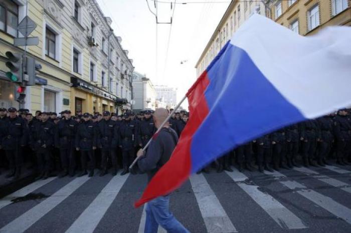 A man with a Russian flag walks past a riot police line standing guard during an anti-war rally in Moscow, September 21, 2014.