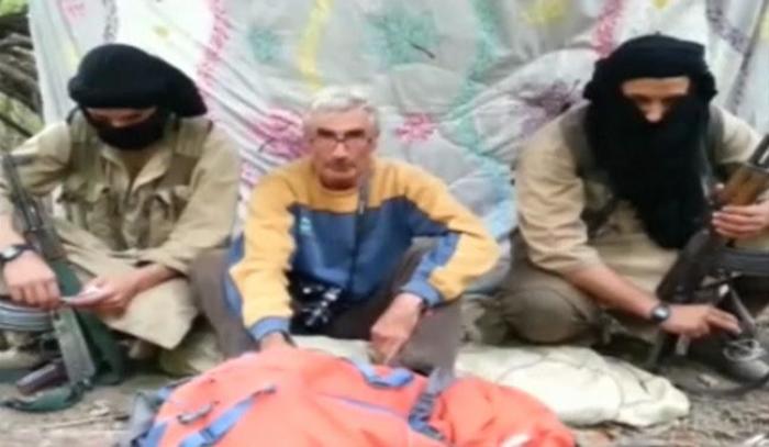 A man who identified himself as Herve Gourdel (C) speaks as he sits in between two masked armed gunmen in this still image taken from video which was published on the Internet on September 22, 2014.