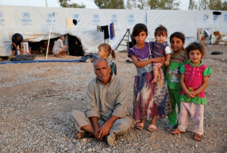 A displaced Iraqi man, who fled from the Islamic State violence in Mosul, poses for the camera with his daughters at Baherka refugee camp in Erbil, September 19, 2014.