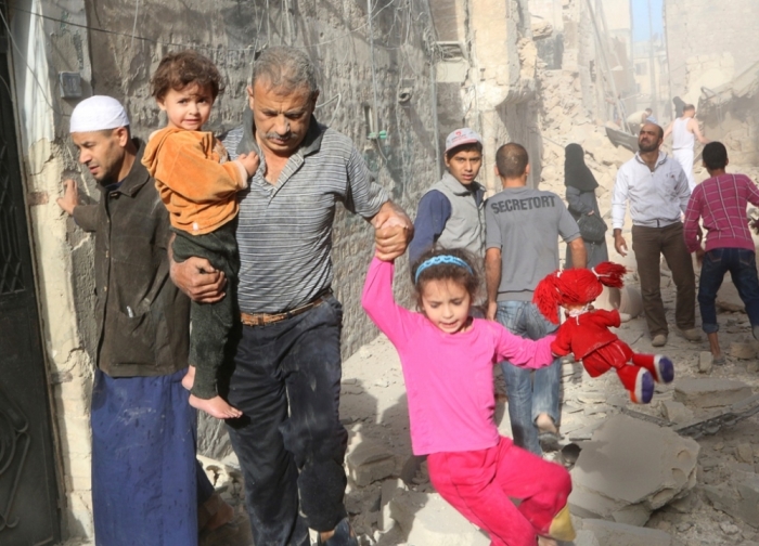 A man holds children as they walk away from a site hit by what activists was a barrel bomb dropped by forces loyal to Syria's President Bashar al-Assad at Qadi Askar district of Aleppo, September 30, 2014.