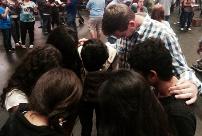 Students pray with a Harvest America volunteer after making professions of faith in Jesus Christ after hearing pastor Greg Laurie share the Gospel with a sold-out crowd of 19,000 for Harvest America at the American Airlines Center and Victory Park in Dallas, Texas, Oct. 5, 2014. The students are holding copies of the book, 'Start!: The Bible for New Believers,' by Greg Laurie, that were handed out at the event.
