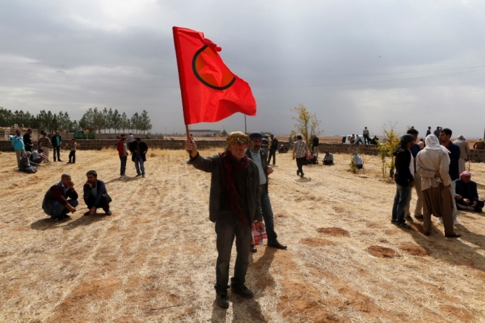 A man holds a flag during the funeral of four Kurdish women fighters killed during clashes against Islamic State fighters in Kobani at a cemetery in the southeastern town of Suruc, Sanliurfa province, October 14, 2014. A senior Iraqi Kurdish official said on Tuesday that Iraq's Kurdistan Regional Government had provided military assistance to Syrian Kurdish forces battling Islamic State fighters in the town of Kobani.