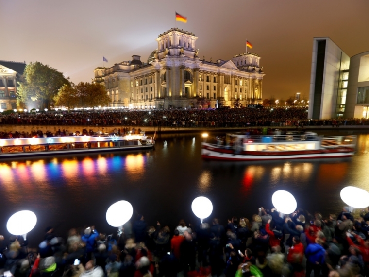 People stand outside the Reichstag lower house of parliament builiding under lit balloons, which are part of the installation 'Lichtgrenze' (Border of Light) in Berlin, November 9, 2014. A part of the inner city of Berlin is being temporarily divided from November 7 to 9, with a light installation featuring 8000 luminous white balloons, following the 9.5-mile (15.3 kmilometre) path the Berlin Wall once occupied, to commemorate the 25th anniversary of the fall of the Wall.