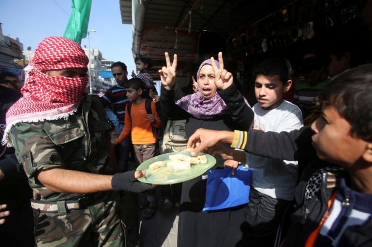 A masked Palestinian distributes sweets as he celebrates with others an attack on a Jerusalem synagogue, in Rafah in the southern Gaza Strip, November 18, 2014. Two Palestinians armed with a meat cleaver and a gun killed four people in a Jerusalem synagogue on Tuesday before being shot dead by police, the deadliest such incident in six years in the holy city amid a surge in religious conflict.
