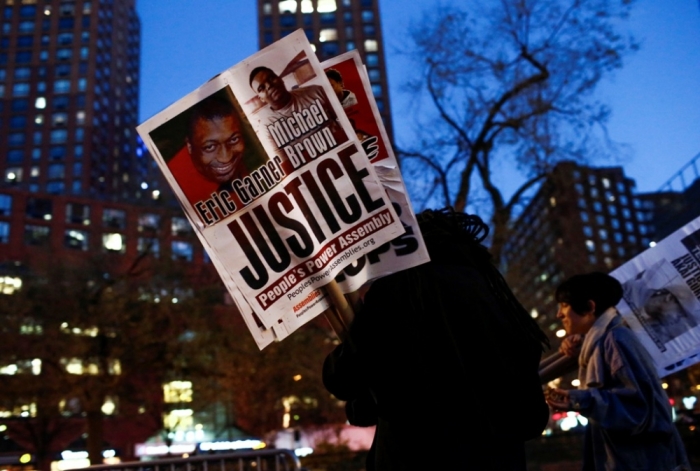 A man holds a sign with images of Eric Garner and Michael Brown as protesters begin to rally in New York, November 24, 2014, after the grand jury reached a decision in the death of 18-year-old Brown in Ferguson, Missouri. The Missouri grand jury has made a decision on whether to indict white police officer Darren Wilson in the August fatal shooting of unarmed black teenager Brown in Ferguson, a killing that sparked angry protests in the St. Louis suburb, prosecutors said on Monday. Garner died in July after being placed in a banned chokehold by a New York City police officer.