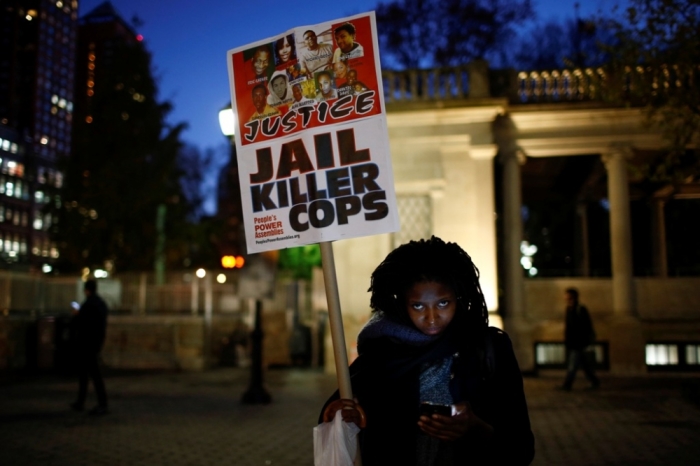 A woman holds a sign with images of Eric Garner and Michael Brown, among others, as protesters begin to rally in New York, November 24, 2014, after the grand jury reached a decision in the death of 18-year-old Brown in Ferguson, Missouri. The Missouri grand jury has made a decision on whether to indict white police officer Darren Wilson in the August fatal shooting of the unarmed black teenager Brown in Ferguson, a killing that sparked angry protests in the St. Louis suburb, prosecutors said on Monday. Garner died in July after being placed in a banned chokehold by a New York City police officer.