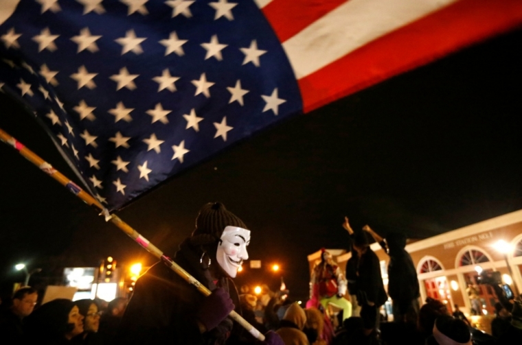 A protester wearing a Guy Fawkes mask carries an American flag outside the Ferguson Police Department in Ferguson, Missouri, November 24, 2014. Missouri Governor Jay Nixon urged people in the St. Louis area to show respect and restraint following a grand jury's decision on whether to criminally charge a white police officer in the August fatal shooting of unarmed black teenager Michael Brown. Prosecutors are set to announce the grand jury's decision at 8 p.m. local time on Monday.