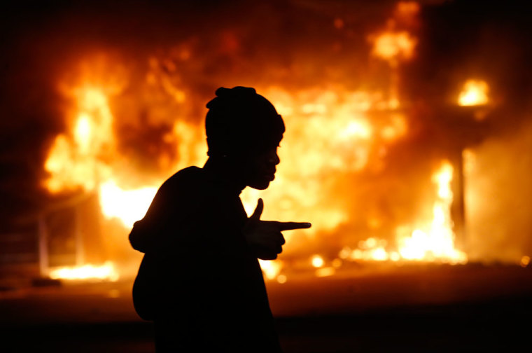 A man walks past a burning building during rioting after a grand jury returned no indictment in the shooting of Michael Brown in Ferguson, Missouri, early November 25, 2014. Gunshots were heard and bottles were thrown as anger rippled through a crowd outside the Ferguson Police Department in suburban St. Louis after authorities on Monday announced that a grand jury voted not to indict a white officer in the August shooting death of an unarmed black teen.