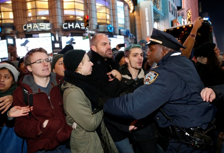 A policeman pushes back demonstrators during a protest over a grand jury decision in the choking case of Eric Garner, in New York, December 4, 2014. U.S. Attorney General Eric Holder on Thursday promised a full investigation into a white New York police officer's role in the choking death of Garner, following a night of protests over a grand jury decision not to bring charges in the incident.