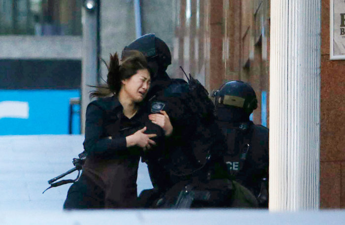 A hostage runs towards a police officer outside Lindt cafe, where other hostages are being held, in Martin Place in central Sydney December 15, 2014. Two more hostages have run out of the cafe at the center of a siege in Sydney, Australia's largest city, according to a Reuters witness at the site. The two women were both wearing aprons indicating they were staff at the Lindt cafe where a gunman has been holding an unknown number of hostages for several hours. Three men had earlier run out of the cafe.