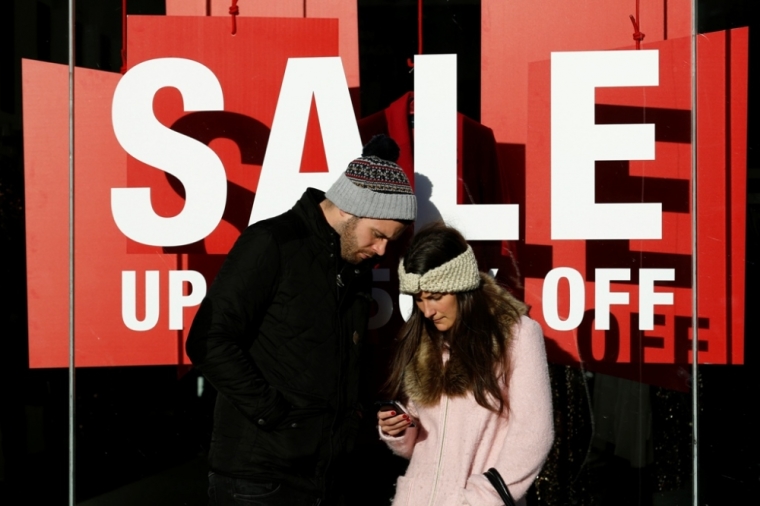 A couple stand outside a shop with an early sale during the final weekend of shopping before Christmas in London, England, December 20, 2014.