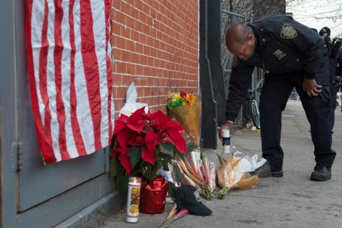 A police officer lays flowers at a makeshift memorial at the scene were two police officers were shot dead in the Brooklyn borough of New York, December 21, 2014. The officers, Wenjian Liu and Rafael Ramos were shot and killed as they sat in a marked squad car in Brooklyn on Saturday afternoon, New York Police Commissioner William Bratton said. The suspect in the shooting then shot and killed himself, Bratton said at a news conference at the Brooklyn hospital where the two officers were taken.