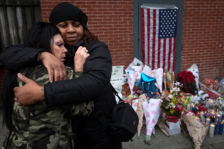 Donna Salvaggio (L) and a woman who gave her name as Reverend Jordan hug at a makeshift memorial at the site where two police officers were shot in the head in the Brooklyn borough of New York, December 21, 2014. The officers, Wenjian Liu and Rafael Ramos were shot and killed as they sat in a marked squad car in Brooklyn on Saturday afternoon, New York Police Commissioner William Bratton said. The suspect in the shooting then shot and killed himself, Bratton said at a news conference at the Brooklyn hospital where the two officers were taken.
