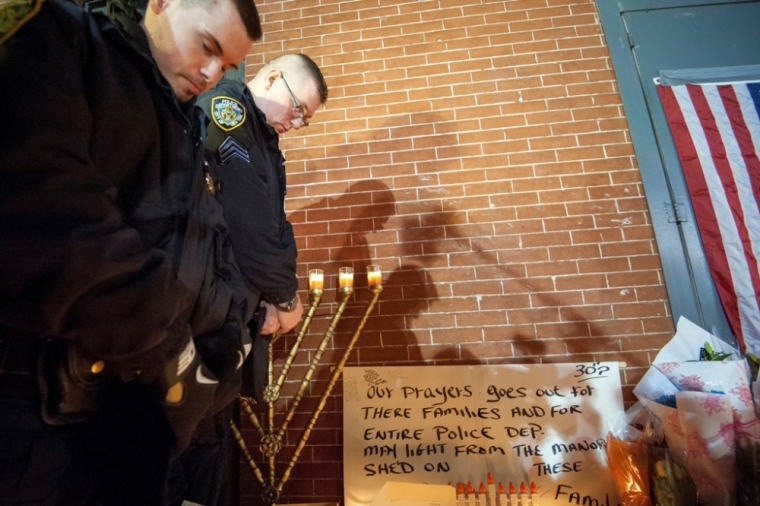 New York Police Department (NYPD) officers stand over a makeshift memorial during a prayer vigil at the site two police officers were fatally shot in the Brooklyn borough of New York, December 21, 2014. New York Mayor Bill de Blasio faced the biggest crisis of his time in office on Sunday following the fatal shooting of two police officers, in an attack intended as retribution for recent U.S. police killings of unarmed black men. Police said the daylight Saturday shooting was the work of a 28-year-old black man who traveled from Baltimore that day after shooting and wounding his girlfriend, having warned on social media that he planned to be 'putting wings on pigs,' using an anti-police slur.