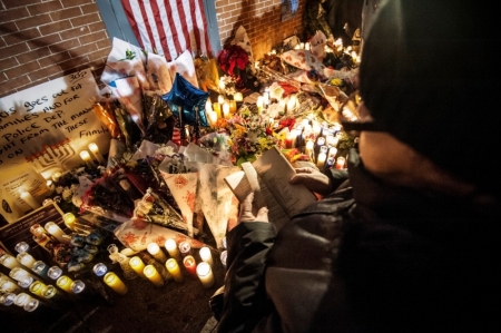 A woman recites from a Bible while standing over a makeshift memorial during a prayer vigil at the site where two New York Police Department (NYPD) officers were fatally shot in the Brooklyn borough of New York December 21, 2014. New York Mayor Bill de Blasio faced the biggest crisis of his time in office on Sunday following the fatal shooting of two police officers, in an attack intended as retribution for recent U.S. police killings of unarmed black men. Police said the daylight Saturday shooting was the work of a 28-year-old black man who traveled from Baltimore that day after shooting and wounding his girlfriend, having warned on social media that he planned to be "putting wings on pigs," using an anti-police slur.