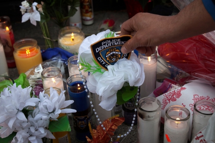 Miguel Esteves places an NYPD badge on a makeshift memorial at the site where two police officers were shot in the head in the Brooklyn borough of New York, December 21, 2014. The officers, Wenjian Liu and Rafael Ramos were shot and killed as they sat in a marked squad car in Brooklyn on Saturday afternoon, New York Police Commissioner William Bratton said. The suspect in the shooting then shot and killed himself, Bratton said at a news conference at the Brooklyn hospital where the two officers were taken.