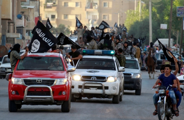 Militant Islamist fighters waving flags, travel in vehicles as they take part in a military parade along the streets of Syria's northern Raqqa province, June 30, 2014.