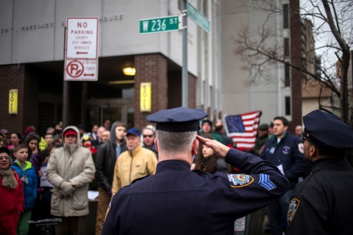 A New York Police Department officer salutes the American flag as residents gather to show their support for policemen, two days after officers Wenjian Liu and Rafael Ramos were shot and killed as they sat in a marked squad car in Brooklyn on Saturday, outside the 50th Precinct Station House in Bronx borough of New York, December 22, 2014. New York City's police commissioner urged an easing of tensions on Monday after some in his force, responding to the fatal shooting of two officers, accused Mayor Bill de Blasio of being insufficiently supportive of police. The U.S. Justice Department on Monday condemned Saturday's attack in which a 28-year-old man with a troubled history killed the two officers in their patrol car to avenge the killings by white officers of unarmed black men in Ferguson, Mo., and New York City.