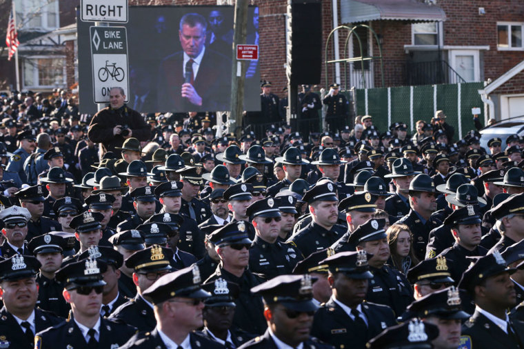 Law enforcement officers turn their backs on a live video monitor showing New York City Mayor Bill de Blasio as he speaks at the funeral of slain New York Police Department (NYPD) officer Rafael Ramos near Christ Tabernacle Church in the Queens borough of New York December 27, 2014. Tens of thousands of police and other mourners filled a New York City church and surrounding streets for the funeral on Saturday of one of two police officers ambushed by a gunman who said he was avenging the killing of unarmed black men by police. Singled out for their uniforms, the deaths of Rafael Ramos and his partner Wenjian Liu have become a rallying point for police and their supporters around the country, beleaguered by months of street rallies by protesters who say police practices are marked by racism.