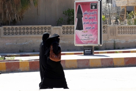 Veiled women walk past a billboard that carries a verse from the Quran urging women to wear a hijab in the northern province of Raqqa, March 31, 2014. The Islamic State in Iraq and the Levant has imposed sweeping restrictions on personal freedoms in the northern province of Raqqa. Among the restrictions, Women must wear the niqab, or full face veil, in public or face unspecified punishments "in accordance with sharia", or Islamic law.