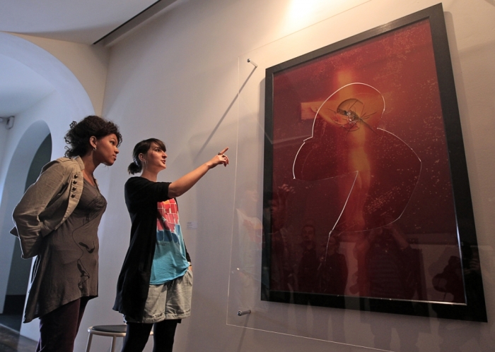 Visitors look at 'Piss Christ,' a piece of art by U.S. artist Andres Serrano, partially destroyed by catholic activists in Avignon, April 19, 2011. The Piss Christ created in 1987, is a photography representing a small plastic crucifix submerged in a glass of the artist's urine.