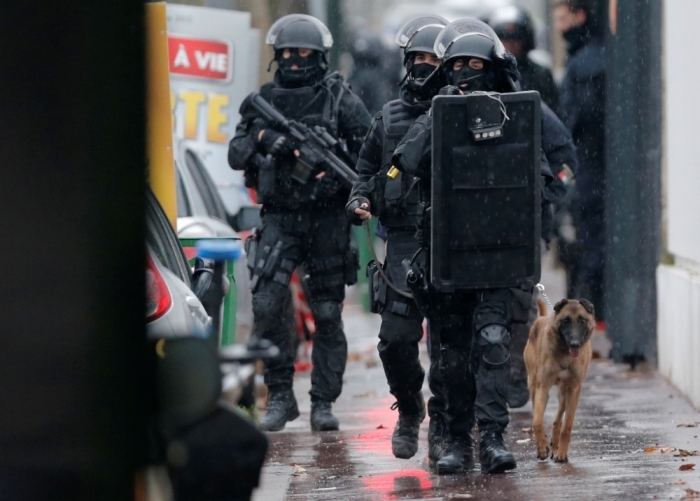 Armed French intervention police walk with a sniffer dog are seen at the scene of a shooting in the street of Montrouge near Paris, January 8, 2015. A policewoman was killed in a shootout in southern Paris on Thursday, triggering searches in the area as the manhunt widened for two brothers suspected of killing 12 people at a satirical magazine in an apparent Islamist militant strike. Police sources could not immediately confirm a link with the killings at Charlie Hebdo weekly newspaper which marked the worst attack on French soil for decades and which national leaders and allied states described as an assault on democracy.