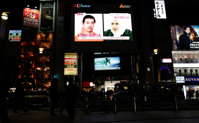 People look at a TV screen broadcasting a news program about Japanese journalist Kenji Goto (top L), who is being held hostage by Islamic State militants, and Sajida al-Rishawi (top R), an Iraqi female prisoner in Jordan, along a street in Tokyo January 29, 2015. An audio message purportedly from Goto being held by Islamic State militants said Jordanian air force pilot Muath al-Kasaesbeh also captured by the group would be killed unless al-Rishawi was released by sunset on Thursday. The message appeared to postpone a previous deadline set on Tuesday in which the journalist Goto, said he would be killed within 24 hours if the Iraqi was not freed.