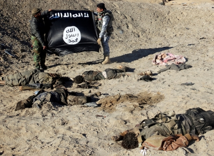 Iraqi security forces hold an Islamic State flag near the bodies of dead members of the Islamic State in the outskirt of Ramadi, December 23, 2014.