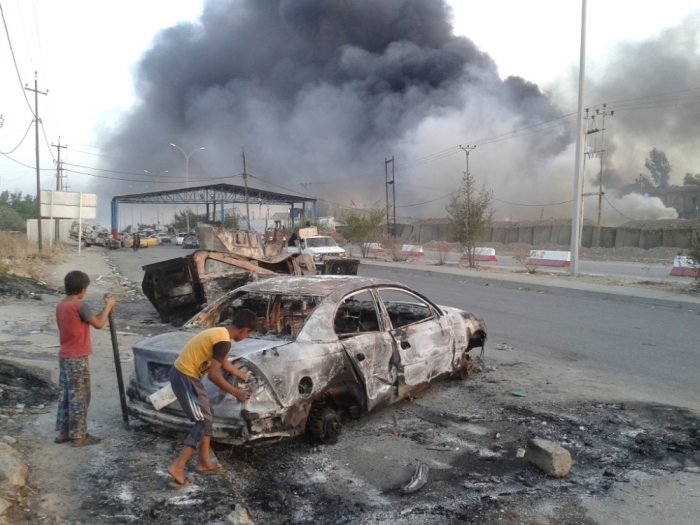 Civilian children stand next to a burnt vehicle during clashes between Iraqi security forces and al Qaeda-linked Islamic State in Iraq and the Levant in the northern Iraq city of Mosul, June 10, 2014. Radical Sunni Muslim insurgents seized control of most of Iraq's second largest city of Mosul early on Tuesday, overrunning a military base and freeing hundreds of prisoners in a spectacular strike against the Shi'ite-led Iraqi government.