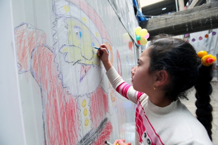 A displaced Iraqi Christian girl who fled from Islamic State militants in Mosul, draws a picture of Santa Claus at a mall still under construction, used as a refugee camp in Arbil, December 24, 2014.