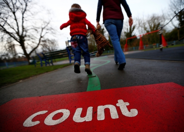A woman walks a child on to a playground in Loughborough, central England, January 29, 2013. Childminders and nurseries in England will be allowed to increase the amount of children that can be looked after per individual, to cut childcare costs and improve standards.