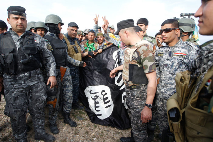 Iraqi police men and Shi'ite fighters hold an Islamist State flag, which they pulled down on the outskirts of al-Alam March 8, 2015. Iraqi security forces and Shi?ite militia fighting the Islamic State took control of the center of a town on the southern outskirts of Saddam Hussein's home city Tikrit on Sunday, security officials said.