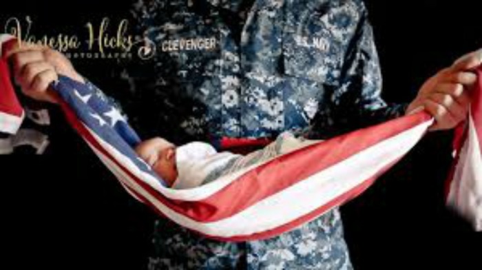 A solider holds his infant child who is wrapped in the American flag.