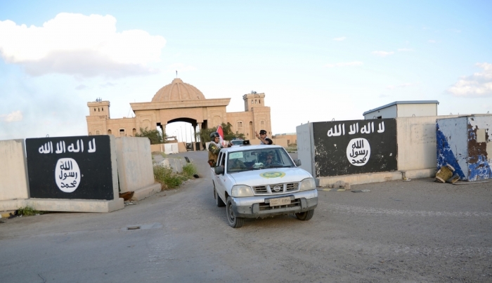 Shiite paramilitary fighters ride a vehicle past a wall painted with the black flag commonly used by Islamic State militants, with the palaces of former Iraqi president Saddam Hussein behind them, in Tikrit, March 31, 2015. Iraqi troops aided by Shi'ite paramilitaries have driven Islamic State out of central Tikrit, Prime Minister Haidar al-Abadi said on Tuesday, but the fight to retake all of Saddam Hussein's home town continued.